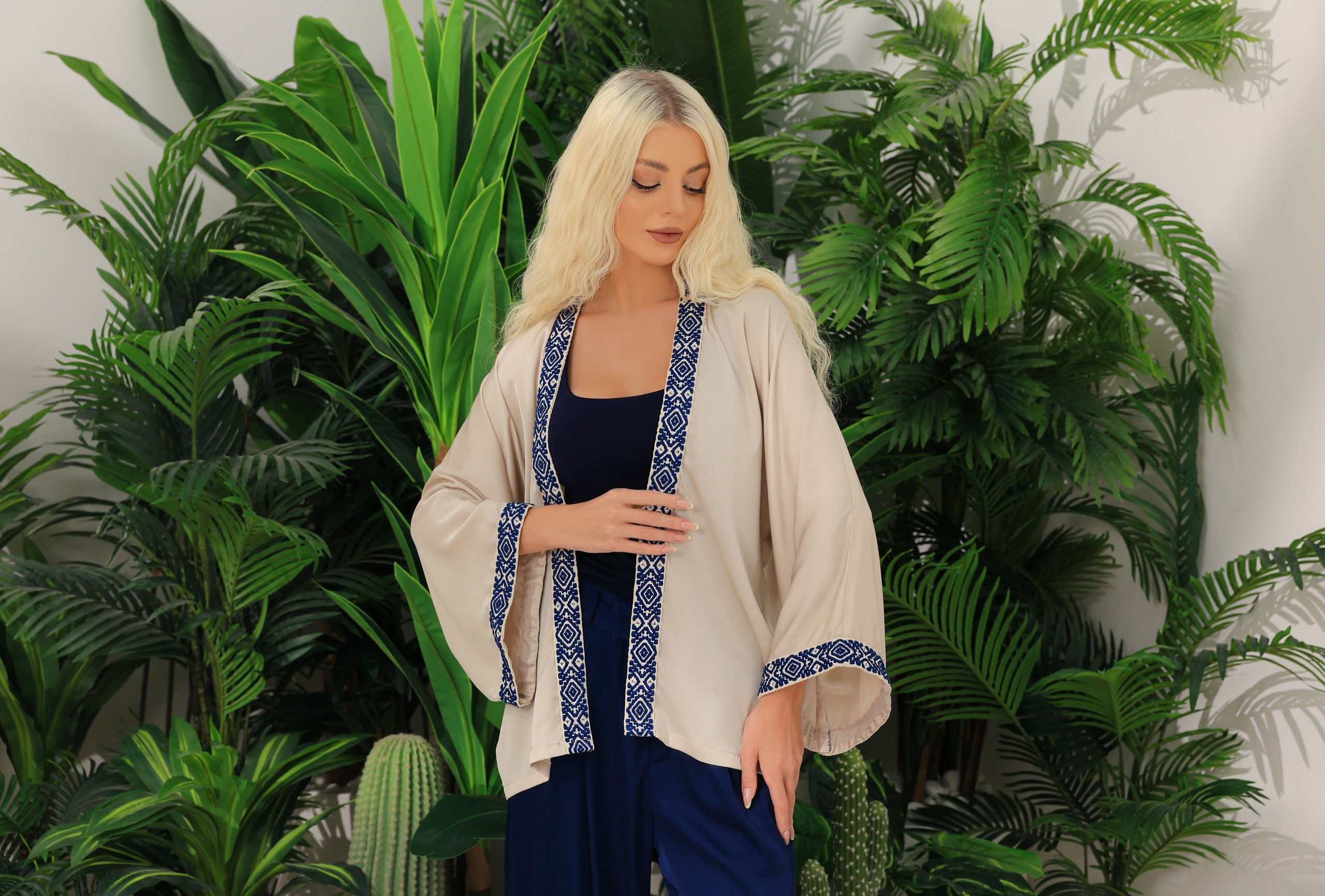 Woman wearing a beige kimono with blue greek accents in a room with green plants