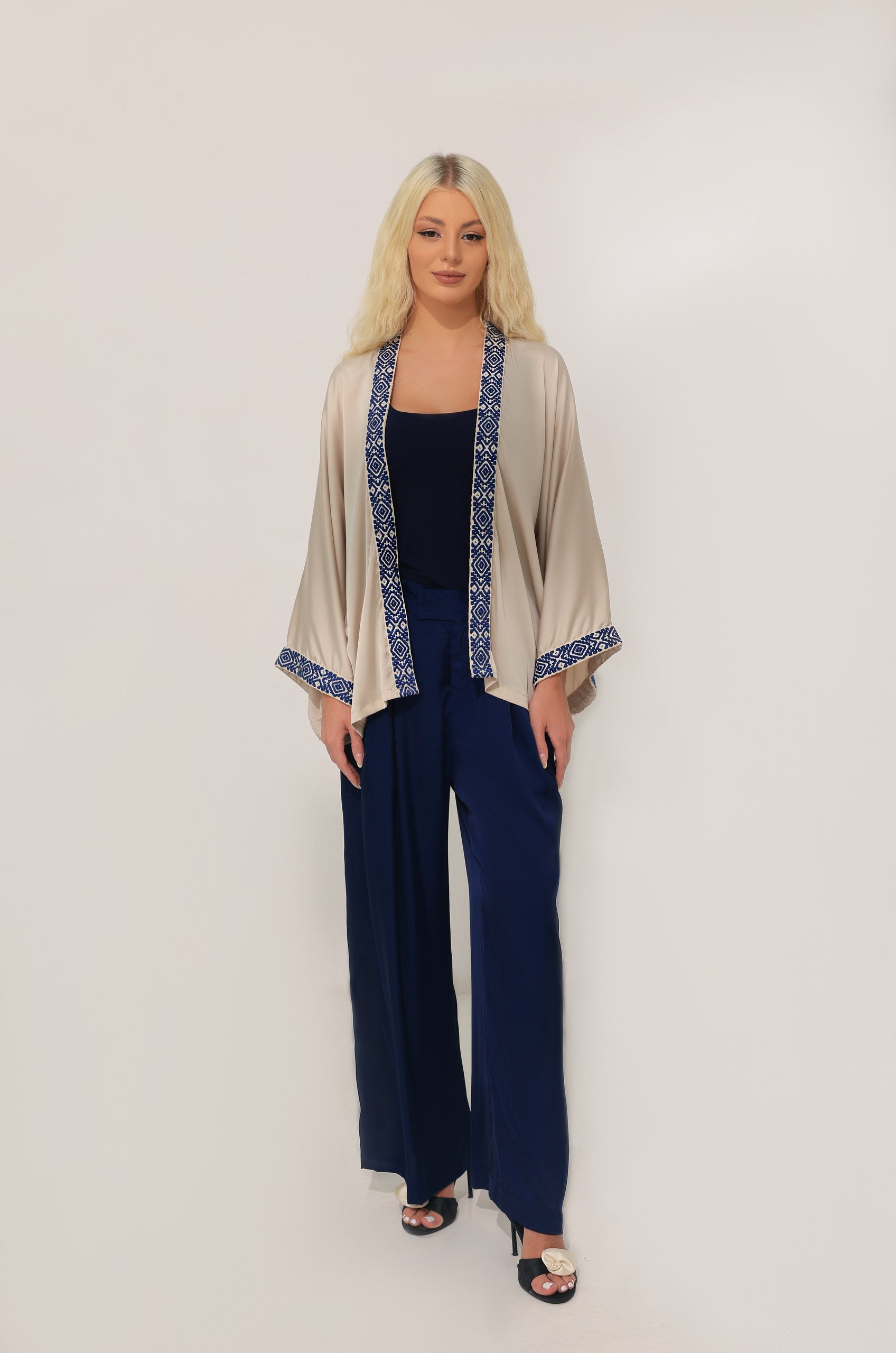 Woman wearing a beige kimono with ancient accents inspired by Greece over a navy outfit on a white background