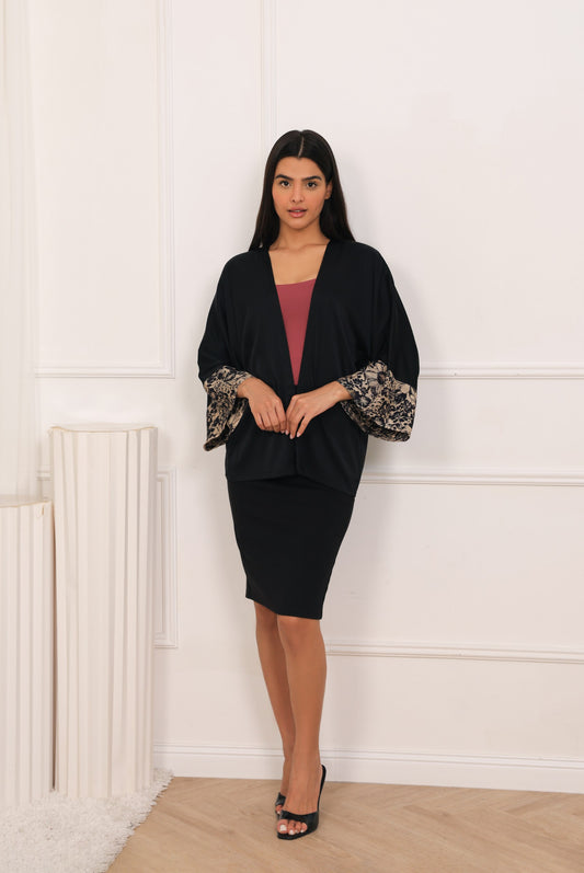 Woman wearing a black cover up kimono with floral sleeves against a white wall