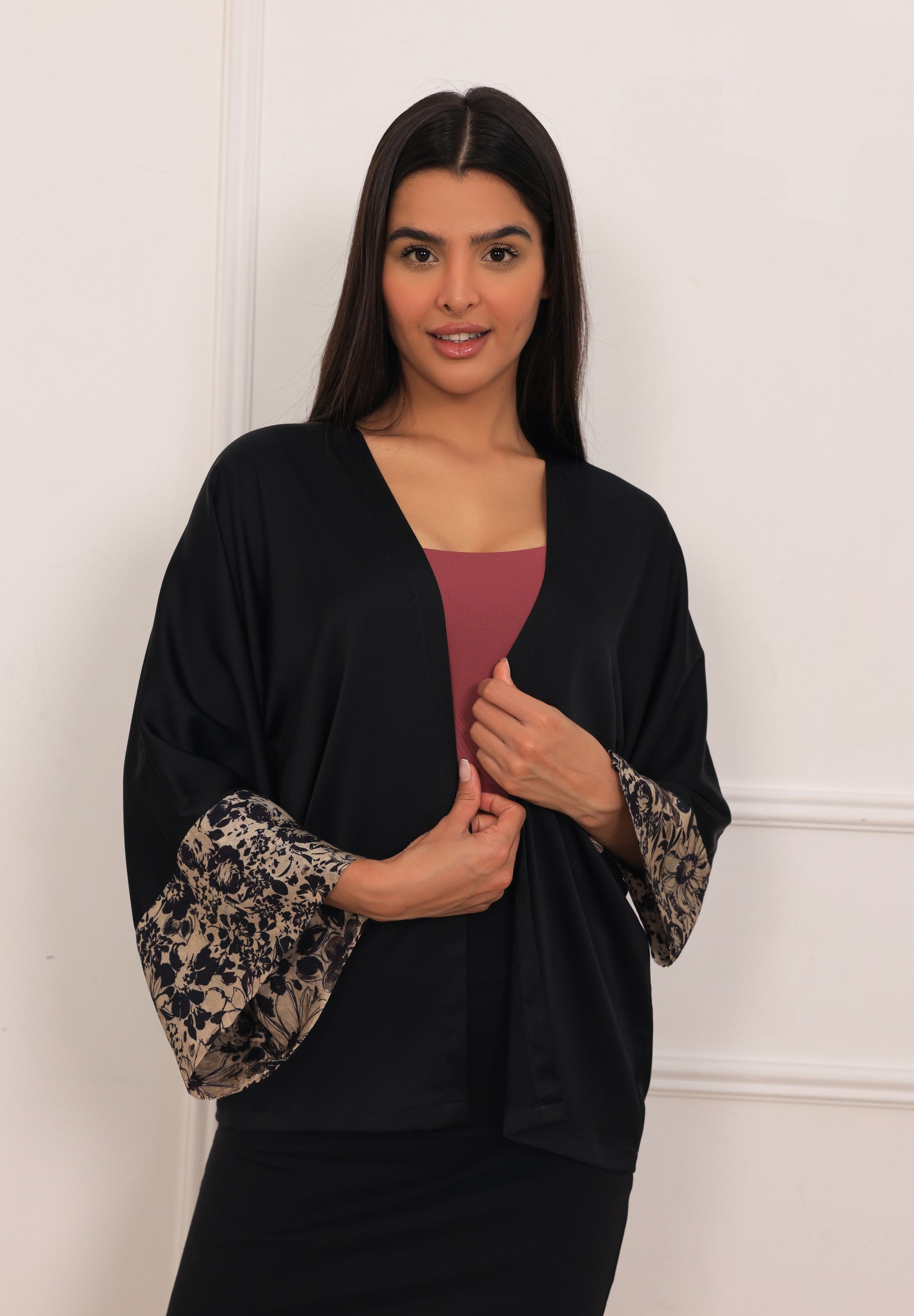 Woman wearing a black kimono-style garment with floral cuffs against a white wall