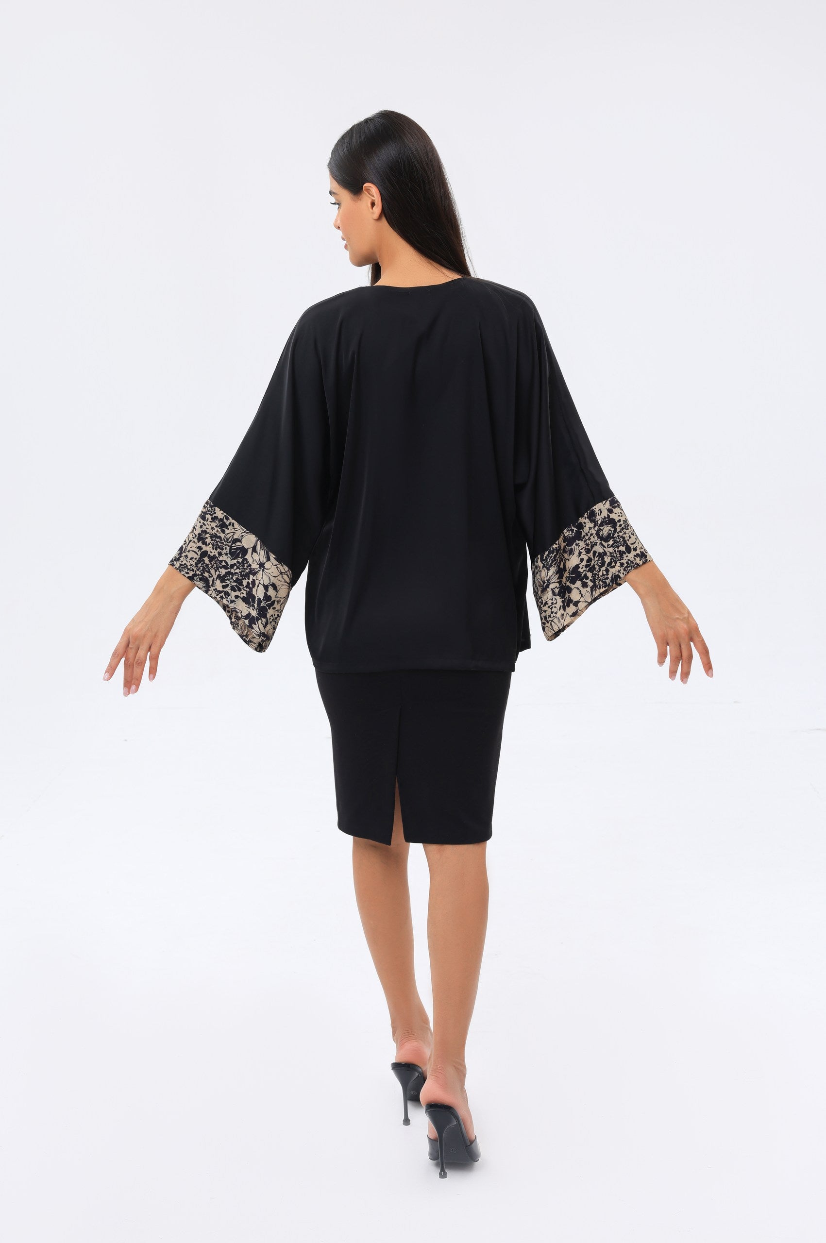 Woman wearing a black kimono cover up with floral cuffs on sleeves against a white background