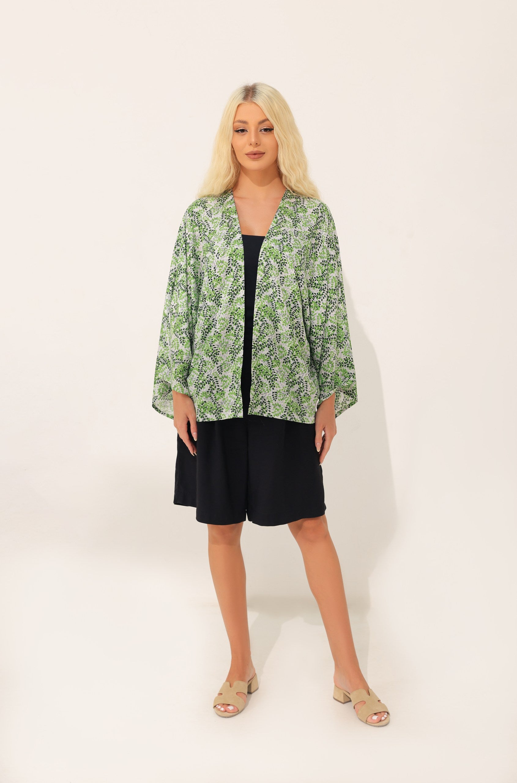 Woman wearing a green patterned kimono over a black shorts on a white background