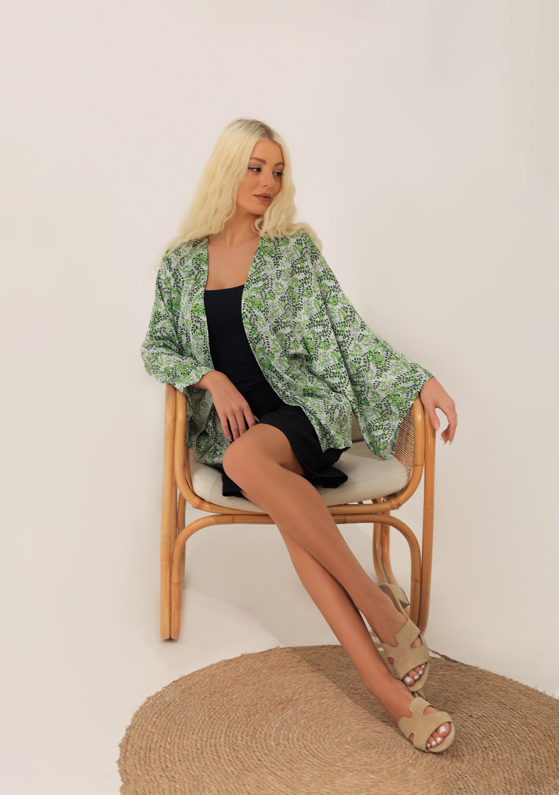 Woman sitting on a chair wearing a green floral modest kimono over a black outfit.