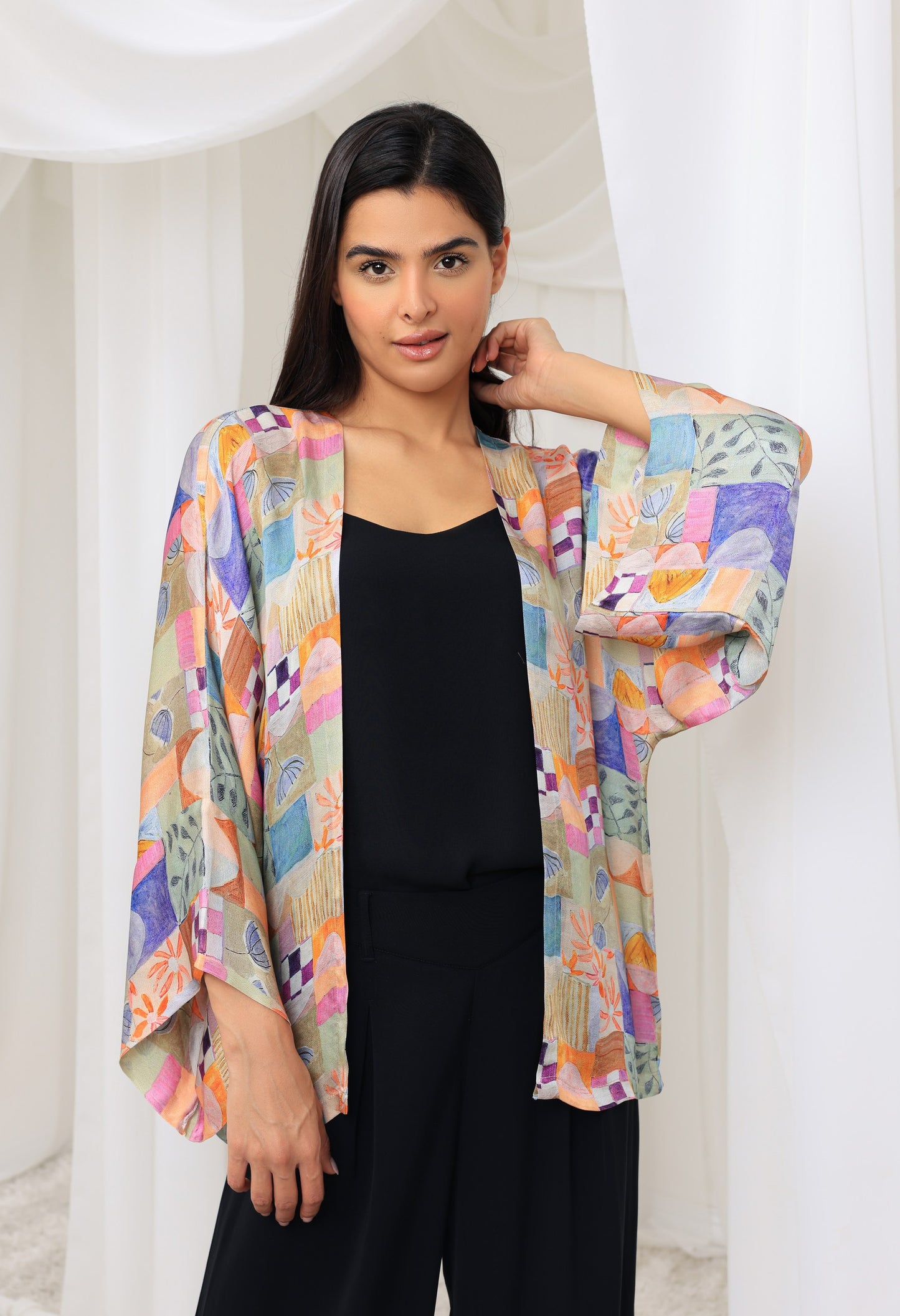 Woman wearing a colorful kimono-cover up over a black outfit on a white background