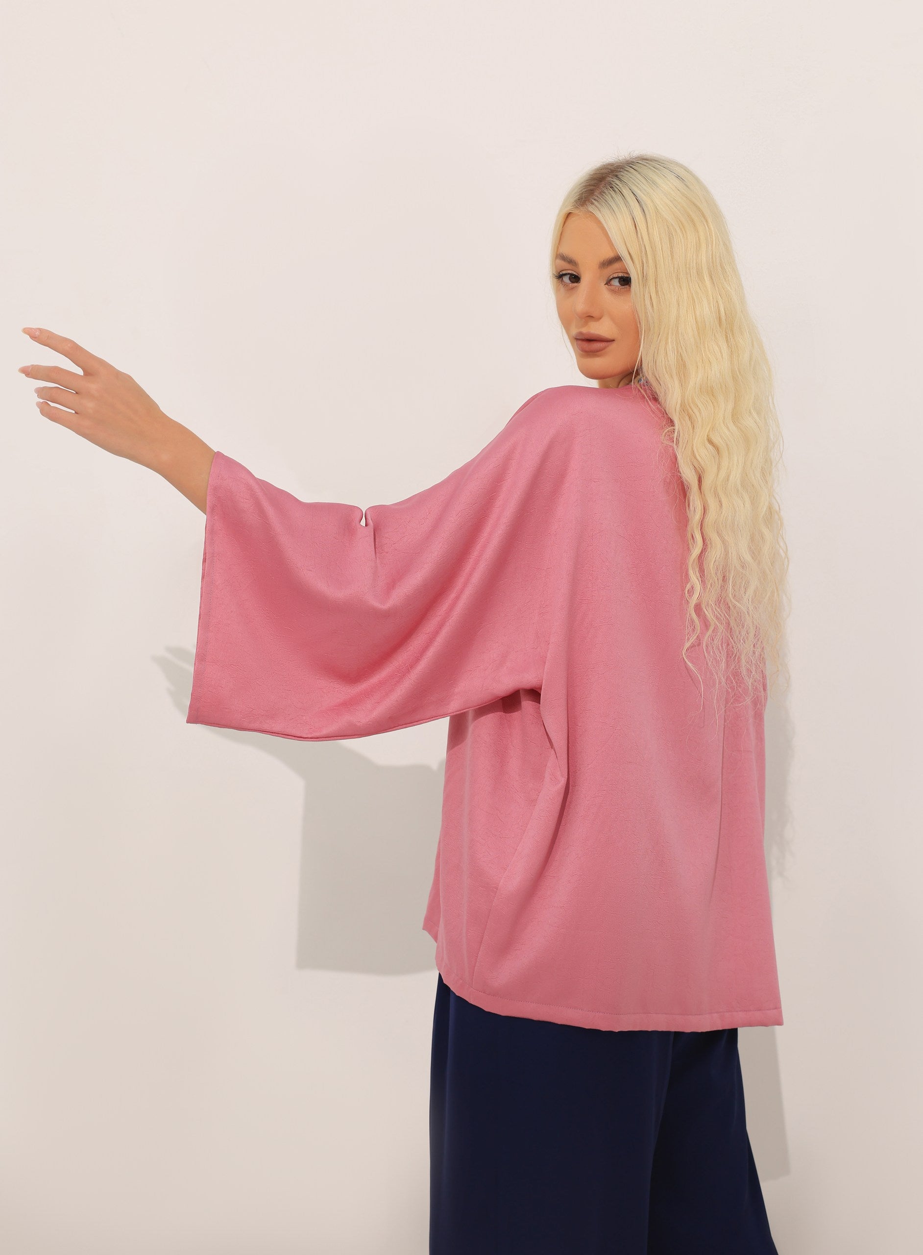 Woman wearing a pink modest kimono with wide sleeves against a white background
