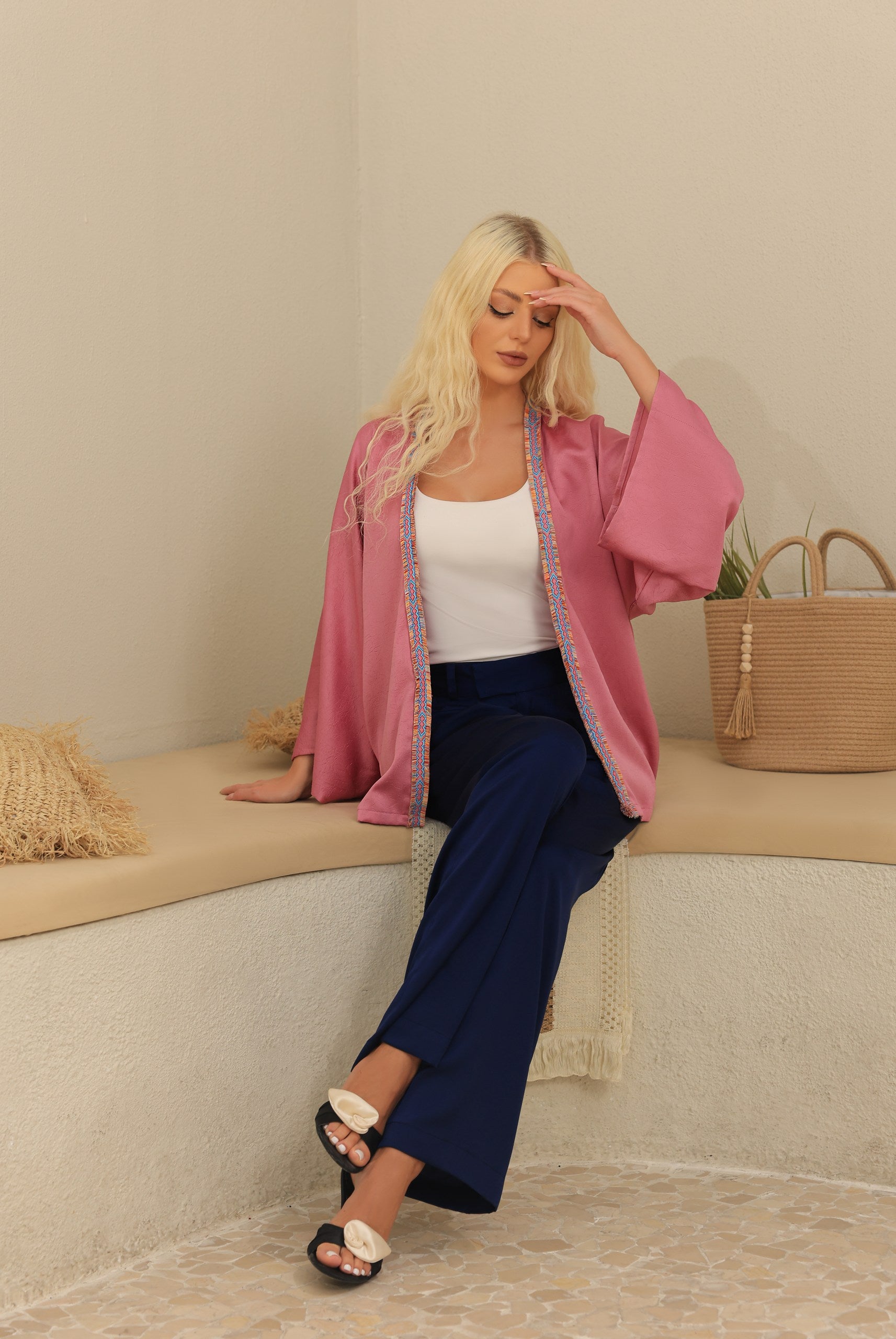 Woman sitting on a bench wearing a pink kimono and blue pants.