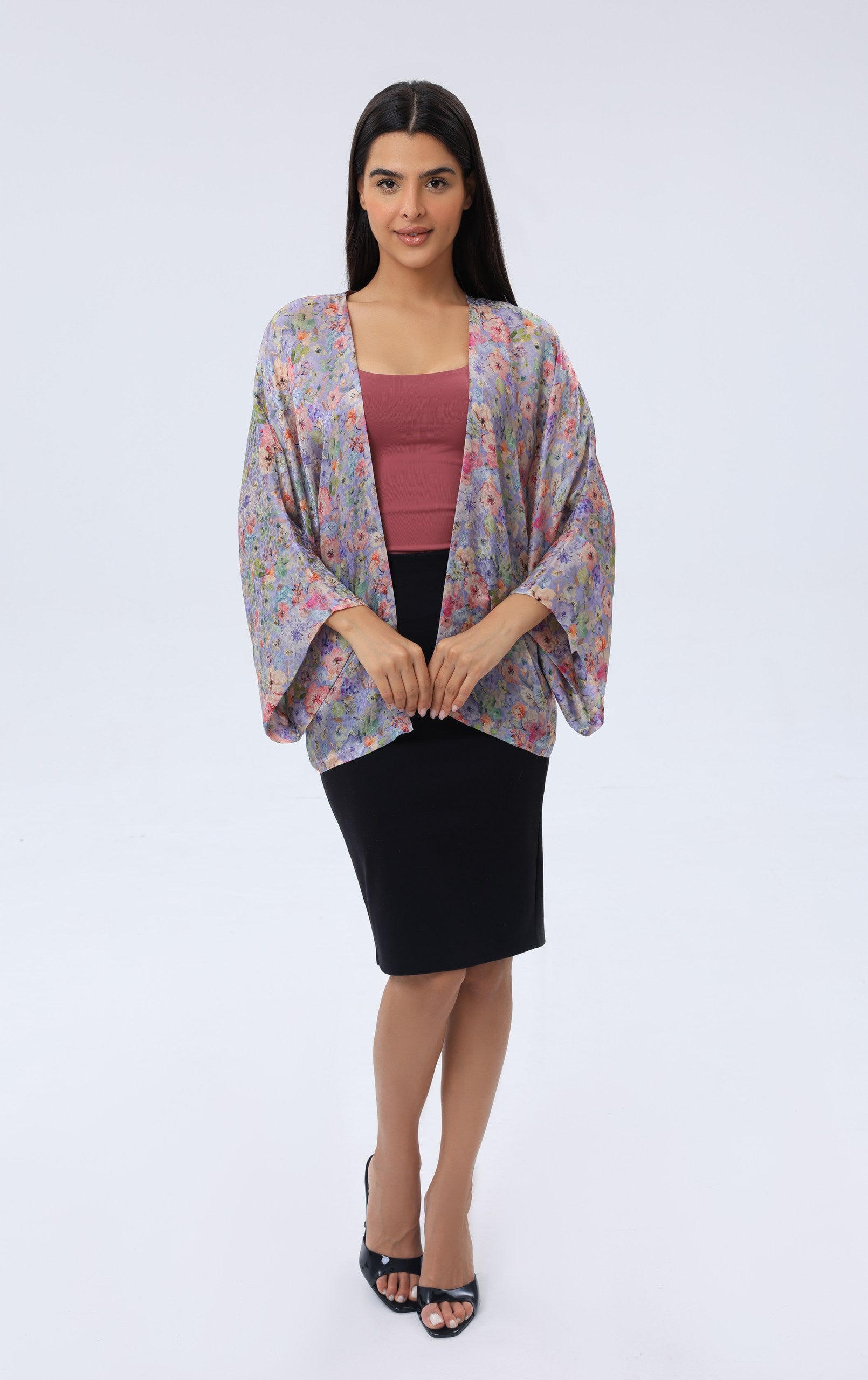 Woman wearing a floral kimono-style cover up over a pink top and black skirt on a white background