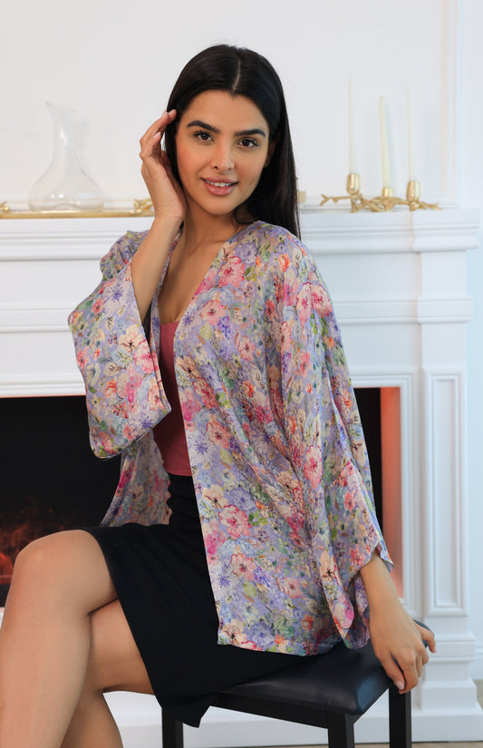 Woman wearing a floral kimono-style garment sitting in a room with a fireplace.