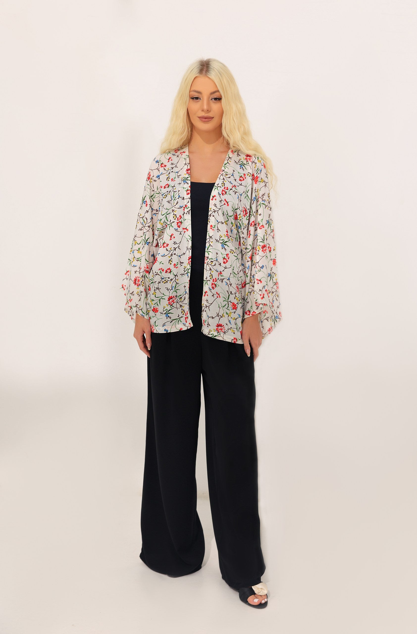 Woman wearing a floral kimono cover up and black pants on a white background