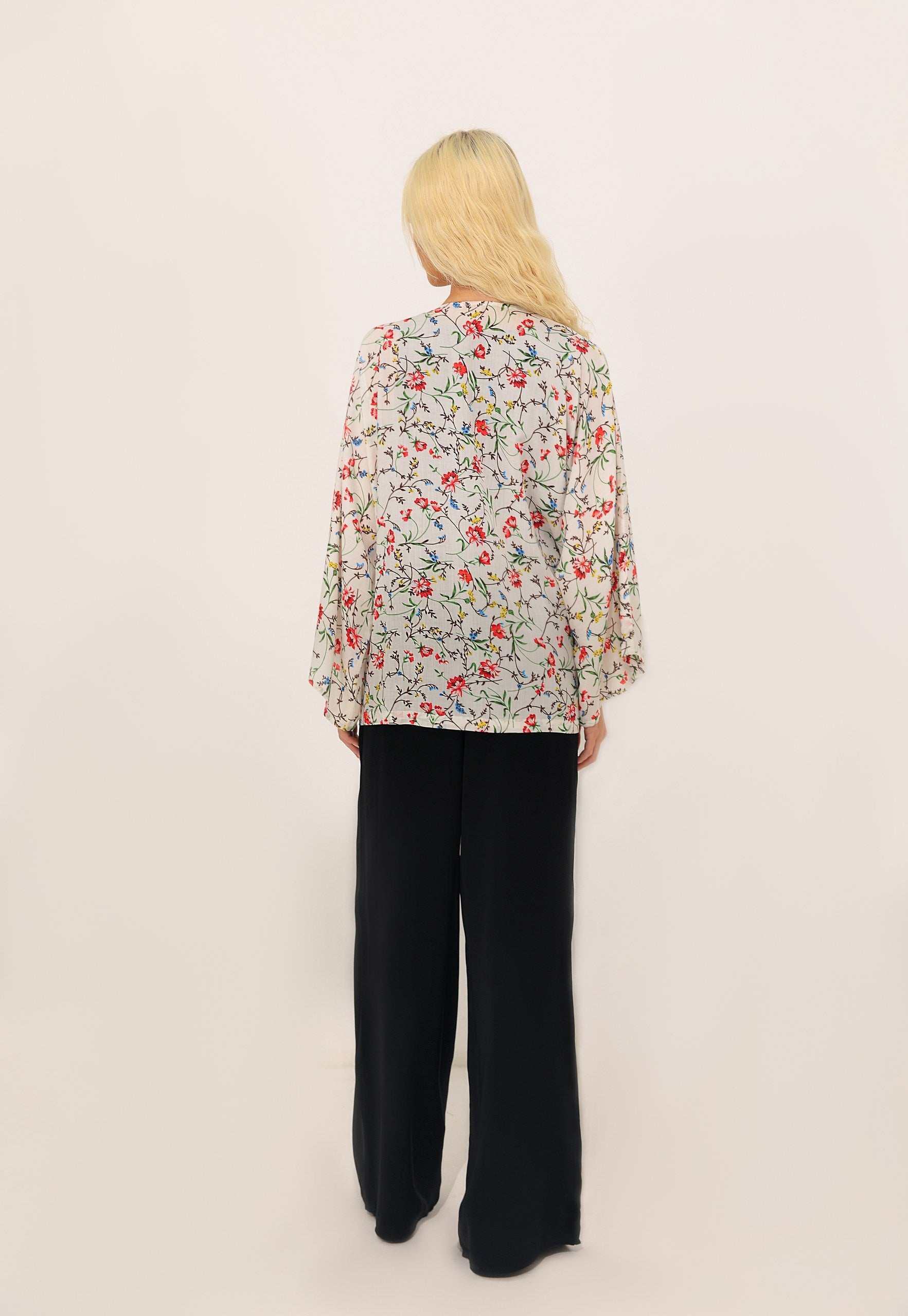 Modest woman wearing a floral cover up and black pants on a white background