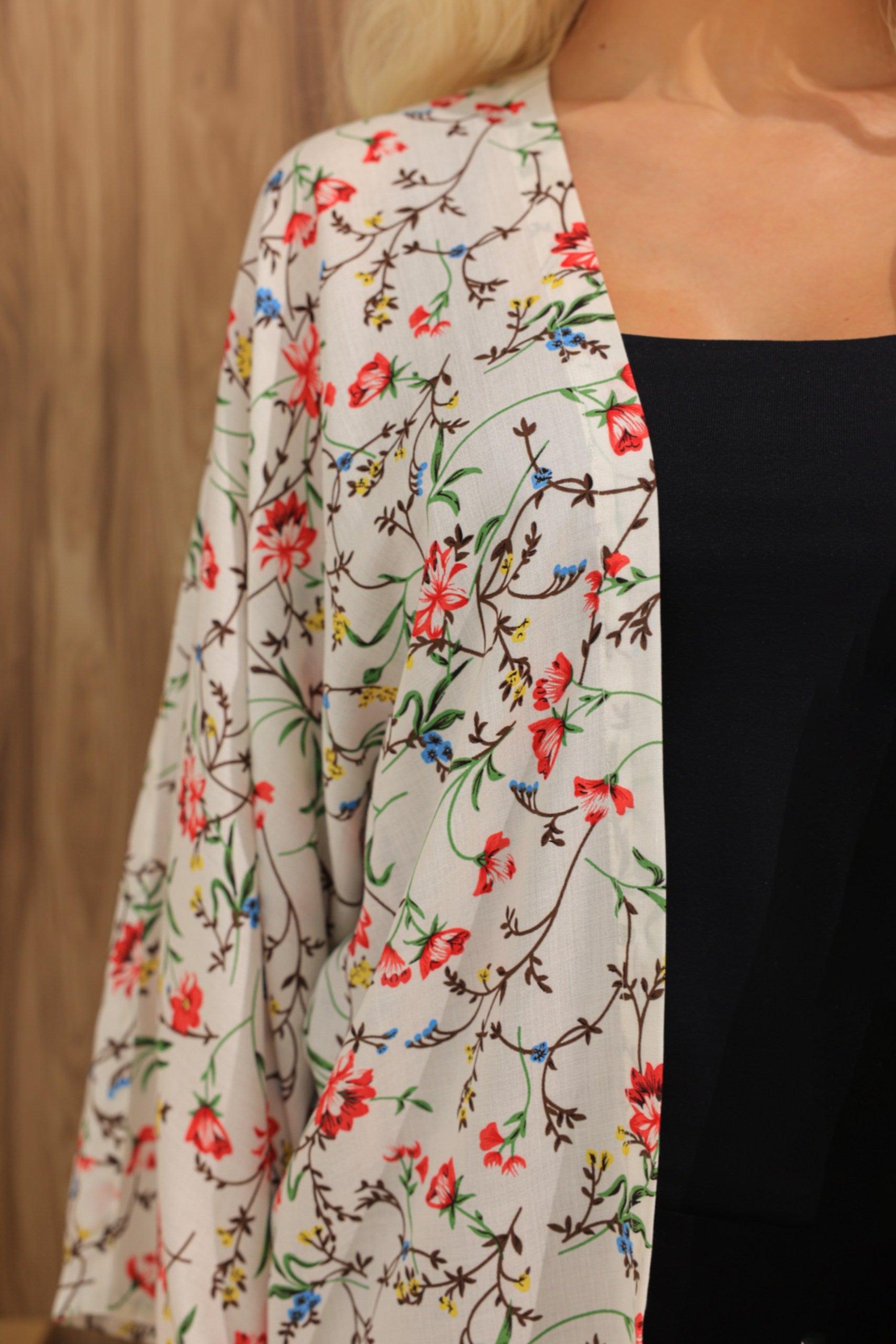 Floral patterned Greece kimono over a black top against a wooden background